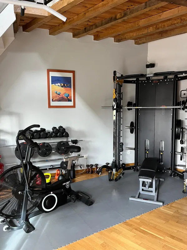 Cage de musculation guidée, banc, haltères et vélo à air sous les poutres de la salle